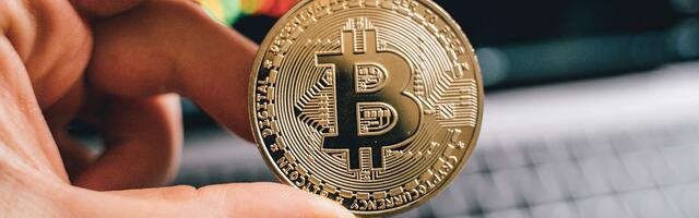 Een fysieke Bitcoin munt die met twee vingers wordt vastgehouden.