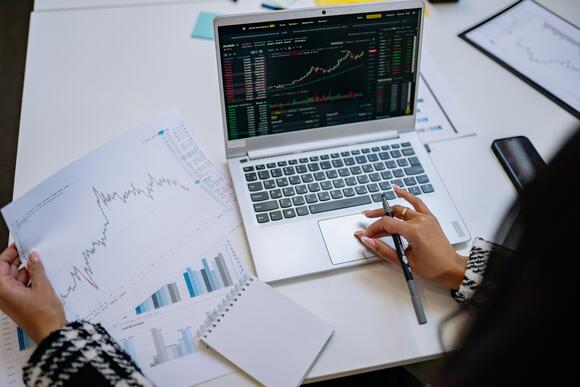 Een vrouw bekijkt via haar laptop en uitgeprinte papieren naar het koersverloop van cryptomunten.