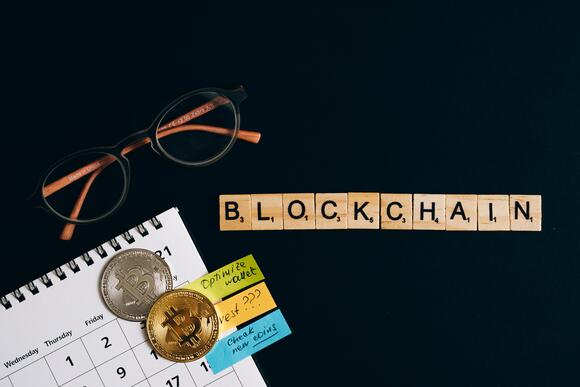 Een afbeelding met munten, een bril en de letters van blockchain.