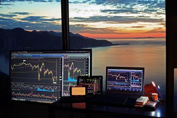 Desktop met daarop verschillende crypto charts, met op de achtergrond een schitterend uitzicht.
