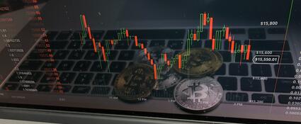 Fysieke Bitcoins die op een laptop liggen met een handelsgrafiek in beeld