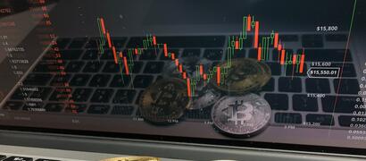 Fysieke Bitcoins die op een laptop liggen met een handelsgrafiek in beeld